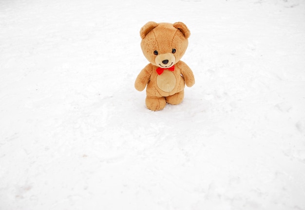 Miś zimą. Koncepcja zima. Brązowy miś z motylkiem na szyi spaceruje po białym śniegu, zimowy dzień. Zabawka na zewnątrz