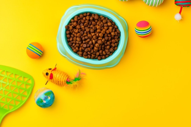 Miska dla kota z suchą karmą i zabawkami na żółtym tle – strzał studyjny