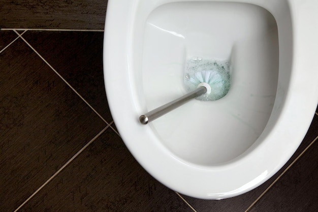 Miska klozetowa ze szczotką toaletową oraz środkiem czyszczącym i dezynfekującym na ciemnym tle płytek ceramicznych