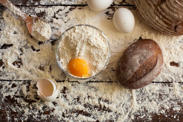 miska mąki pszennej z surowym jajkiem i drewnianą łyżką pełna mąki ładny smaczny chleb i skorupka jajka