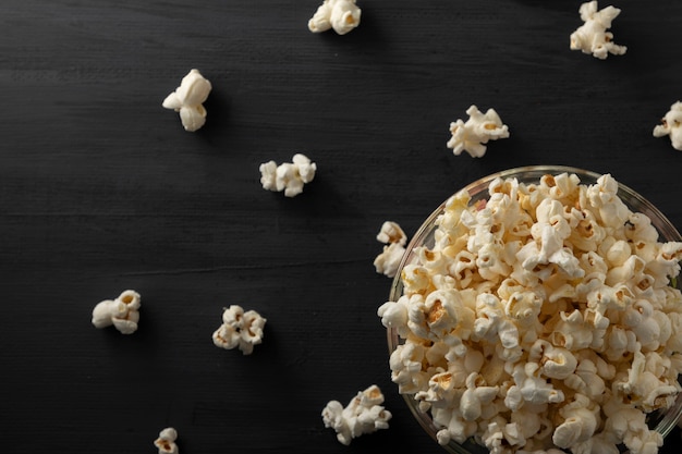 Miska popcornu przewrócona na czarnym drewnianym stole Popcorn rozrzucony na stole