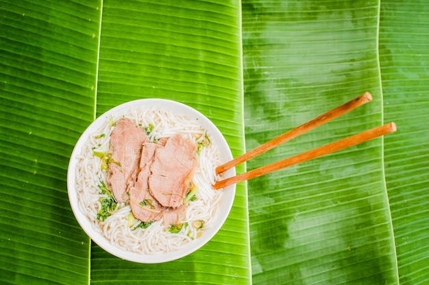 miska tradycyjnej wietnamskiej zupy wołowej Pho Bo na tle liści bananów.