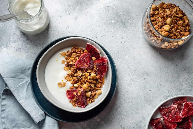 Miska z jogurtem naturalnym, muesli i krwawej pomarańczy na szarej betonowej powierzchni. Czyste jedzenie. obraz poziomy, miejsce kopiowania, płaskie ułożenie.