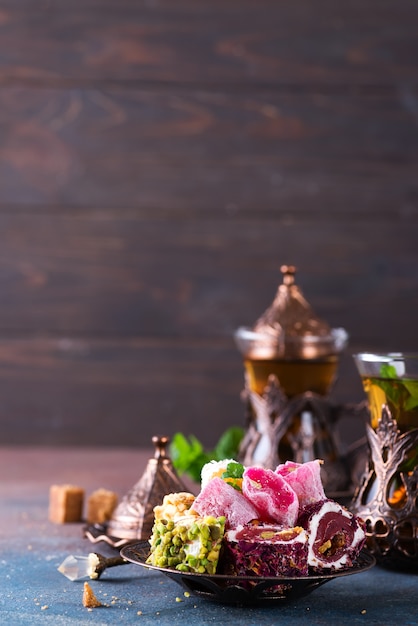Zdjęcie miska z różnymi kawałkami tureckiej rozkoszy lokum i czarnej herbaty z miętą na ciemności.