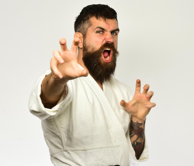Mistrz judo z czarnym pasem ćwiczy postawę ataku lub obrony Mężczyzna z brodą w białym kimonie na białym tle Orientalna koncepcja sportowa Karate man z gniewną twarzą w mundurze