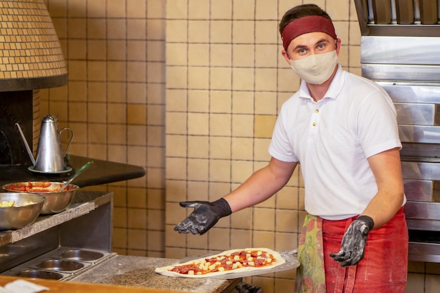 Mistrz Pizzy W Masce I Rękawiczkach Rozkłada Pizzę Na łopacie, żeby Ją Upiec