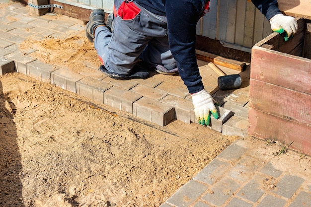 Mistrz układa kostkę brukową warstwami Układanie chodników z cegły ogrodowej przez profesjonalnego brukarza Układanie szarych betonowych płyt chodnikowych na dziedzińcu domu na podstawie z piasku