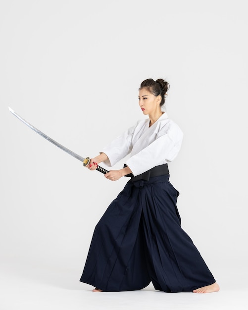Mistrzyni aikido kobieta w tradycyjnym kimono hakama samuraja z czarnym pasem z mieczem katana na białym tle Zdrowy styl życia i sport koncepcja