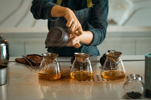 Zdjęcie mistrzyni herbaty wlewa zieloną herbatę z pączkami róży do szklanych kubków przez siatkę