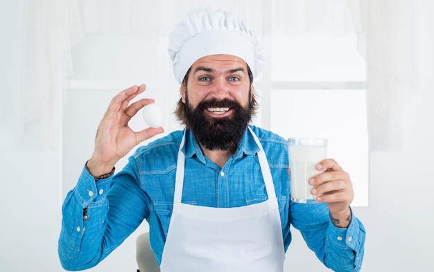 Mleko i jajko mężczyzna kucharz przygotowuje jedzenie w domowej kuchni hipster w fartuchu gotowanie czas posiłku do jedzenia szczęśliwy pieczenia koncepcja sprzątania dojrzały brodaty mężczyzna nosić kapelusz szefa kuchni tylko żywność ekologiczna
