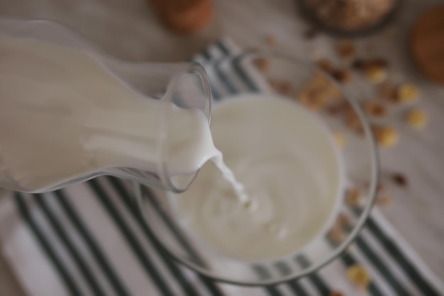 Mleko przelewa się ze szklanej butelki do przezroczystej miski na stole do robienia płatków śniadaniowych