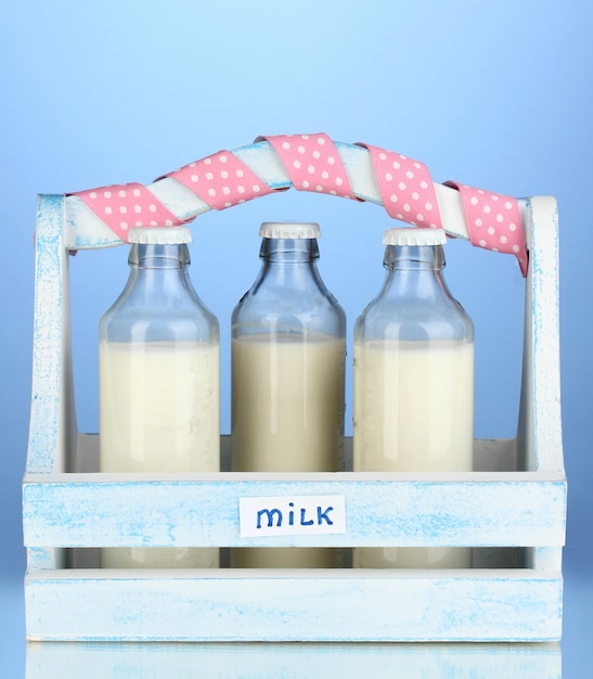 Zdjęcie mleko w butelkach w drewnianym pudełku na niebieskim tle