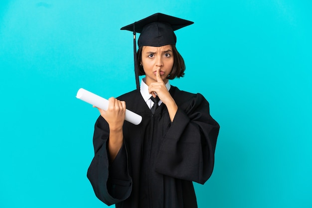 Młoda absolwentka uniwersytetu dziewczyna nad odosobnioną niebieską ścianą wskazującą w bok i wykonującą gest ciszy
