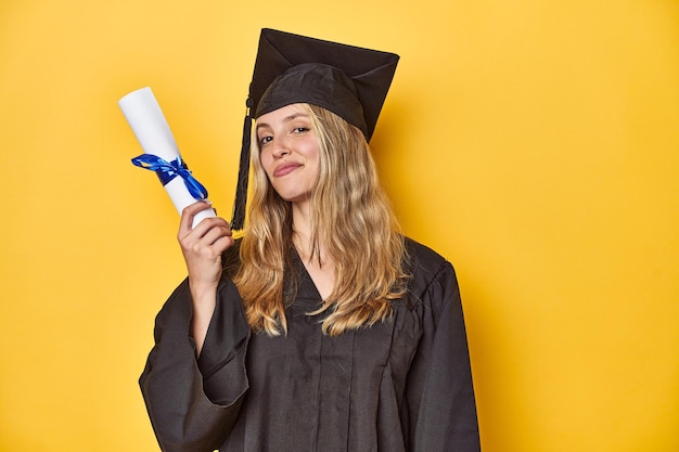 Zdjęcie młoda absolwentka w czapce i szlafroku trzymająca dyplom na żółtym tle studia