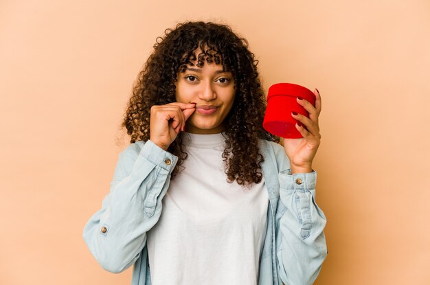 Młoda Afro amerykańska kobieta afro trzyma prezent walentynki z palcami na ustach, zachowując tajemnicę.