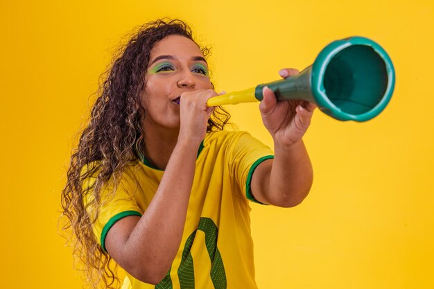 Młoda afro brazylijska cheerleaderka z wuwuzelą na żółtym tle świętuje