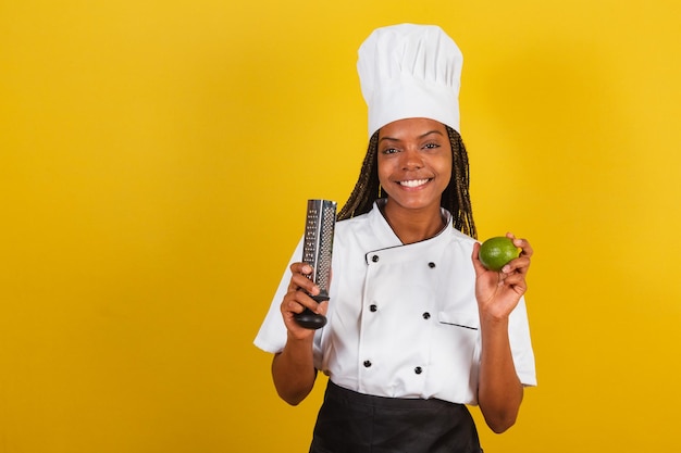 Młoda afro brazylijska kobieta kucharz trzyma cytrynę i tarkę do gotowania