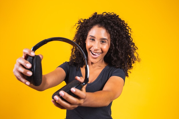 Młoda afro kobieta trzyma słuchawki na żółtym tle. Koncepcja muzyki i rozrywki