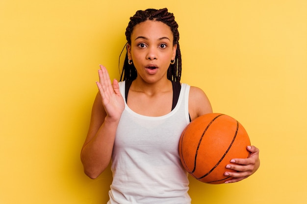 Młoda Afroamerykanin kobieta gra w koszykówkę na białym tle na żółtym tle zaskoczony i zszokowany.