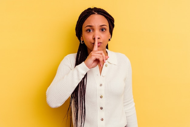Młoda Afroamerykanin kobieta na białym tle na żółtej ścianie, zachowując tajemnicę lub prosząc o ciszę.