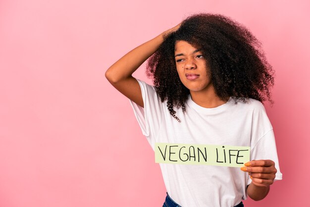 Młoda Afroamerykanin kręcone kobieta trzyma afisz życia wegańskiego dotykając tyłu głowy, myśląc i dokonując wyboru.