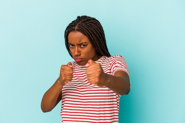Młoda afroamerykanka na białym tle na niebieskim tle rzucająca cios, złość, walka z powodu kłótni, boks.