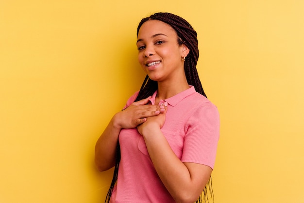 Młoda Afroamerykanka na żółtej ścianie ma przyjazny wyraz, przyciskając dłoń do klatki piersiowej. Koncepcja miłości.