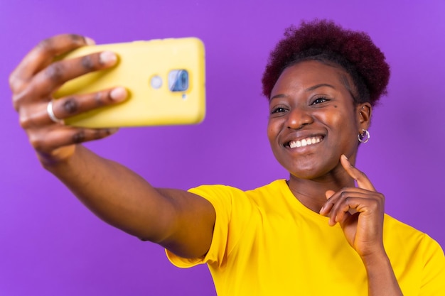 Młoda Afroamerykanka odizolowana na fioletowym tle uśmiecha się i robi selfie w studio