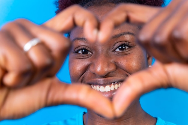 Młoda Afroamerykanka odizolowana na niebieskim tle uśmiecha się i strzela w studio gestów serca