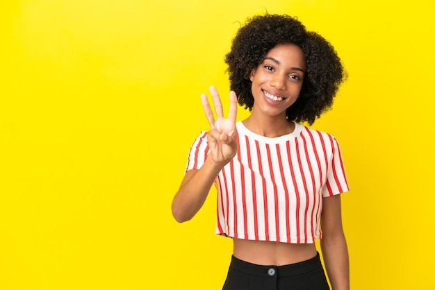 Młoda Afroamerykanka odizolowana na żółtym tle szczęśliwa i licząca trzy palcami