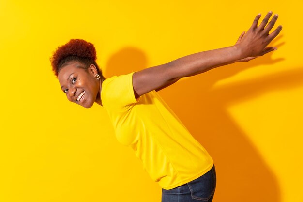 Młoda Afroamerykanka odizolowywająca na żółtym tle uśmiecha się i tańczy studio strzelać