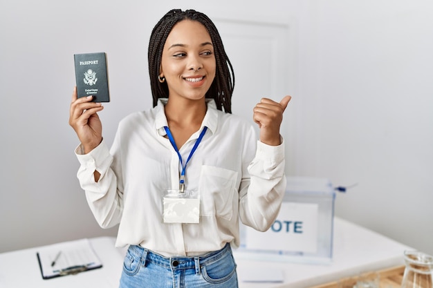 Młoda Afroamerykanka podczas wyborów w kampanii politycznej trzymająca paszport USA wskazująca kciukiem na bok uśmiechnięta zadowolona z otwartymi ustami
