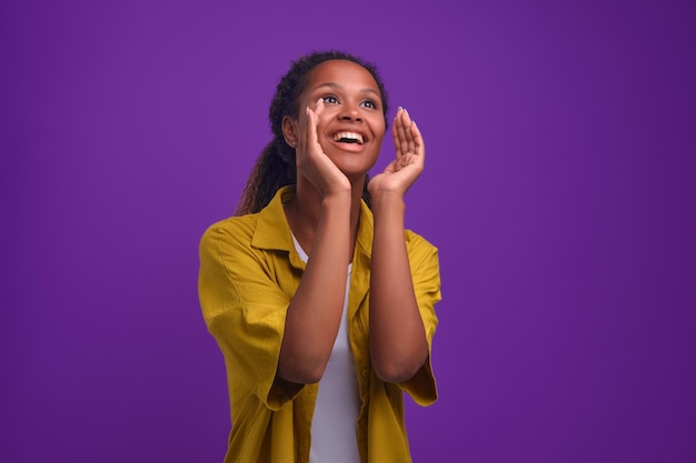Młoda Afroamerykanka podnosi ręce do ust, by głośno wykrzykiwać dobre wieści