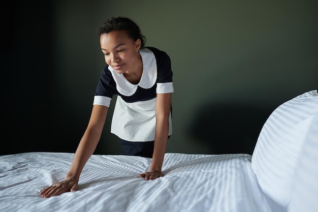 Młoda Afroamerykanka pokojówka pochyla się nad podwójnym łóżkiem
