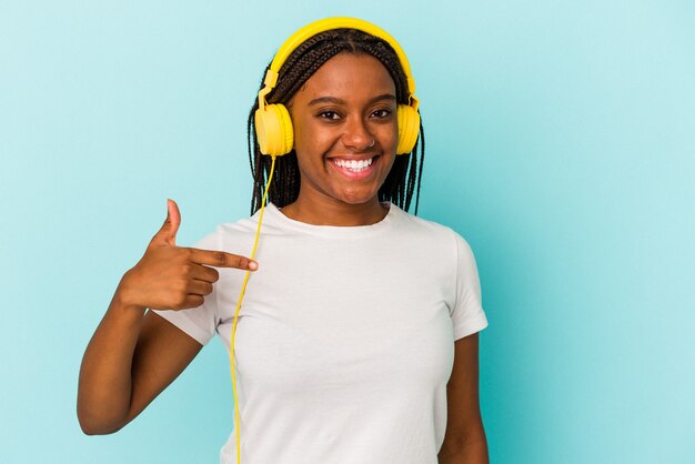 Młoda Afroamerykanka słuchająca muzyki odizolowana na niebieskim tle osoba wskazująca ręcznie na miejsce na koszulkę, dumna i pewna siebie