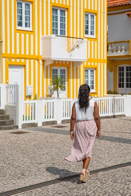 Młoda Afroamerykanka spaceruje po ulicach z kolorowymi domami w paski Costa Nova Aveiro Portugalia