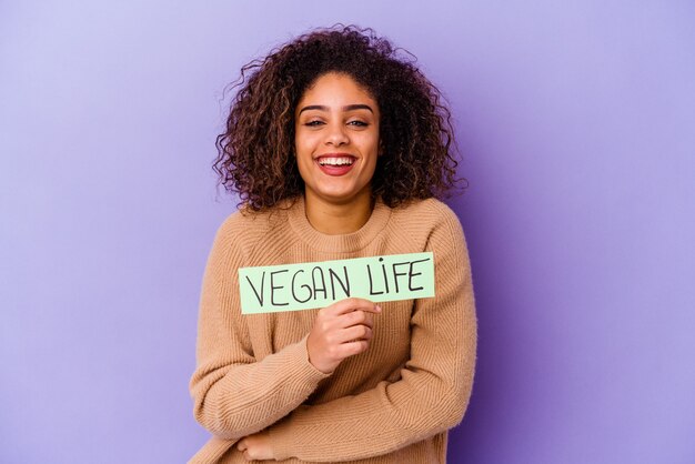 Młoda Afroamerykanka trzyma afisz życia wegańskiego na białym tle, śmiejąc się i bawiąc.