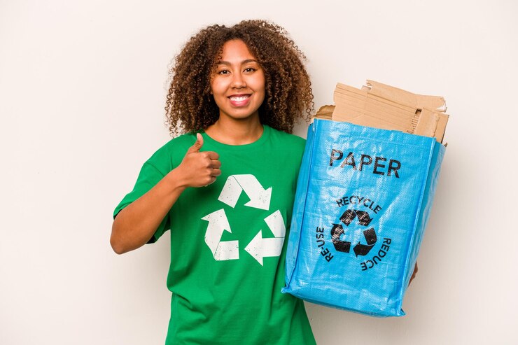 Zdjęcie młoda afroamerykanka trzyma torbę do recyklingu pełną papieru do recyklingu na białym tle, uśmiechając się i unosząc kciuk w górę