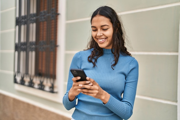 Młoda Afroamerykanka uśmiecha się pewnie za pomocą smartfona na ulicy
