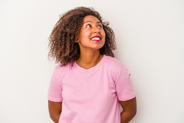 Młoda afroamerykanka z kręconymi włosami na białym tle zrelaksowana i szczęśliwa, śmiejąc się, szyja rozciągnięta pokazując zęby.