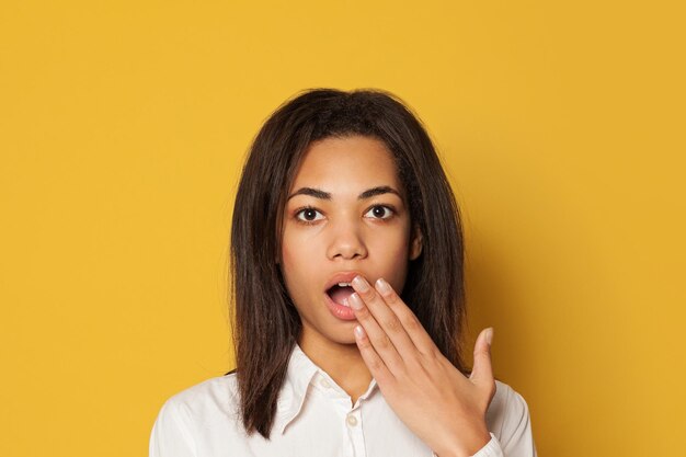 Młoda afroamerykańska kobieta otwiera usta na jasnożółtym tle