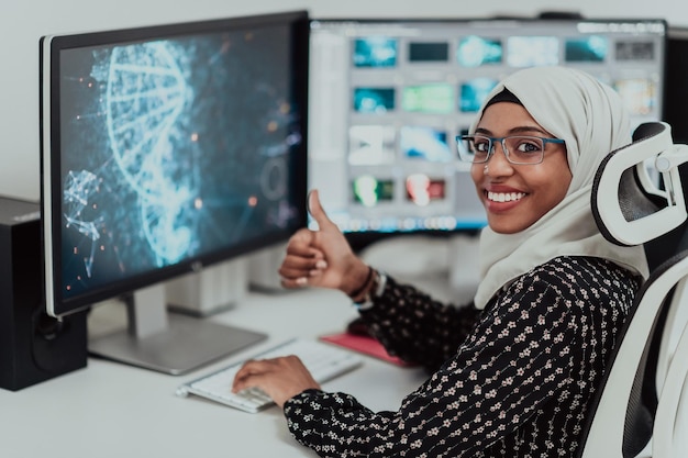 Młoda afroamerykańska nowoczesna muzułmańska bizneswoman w szaliku w kreatywnym, jasnym biurze z dużym ekranem. Zdjęcie wysokiej jakości