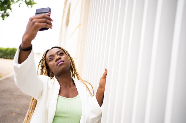 Młoda afrykańska kobieta robi selfie za pomocą telefonu komórkowego, stojąc na zewnątrz