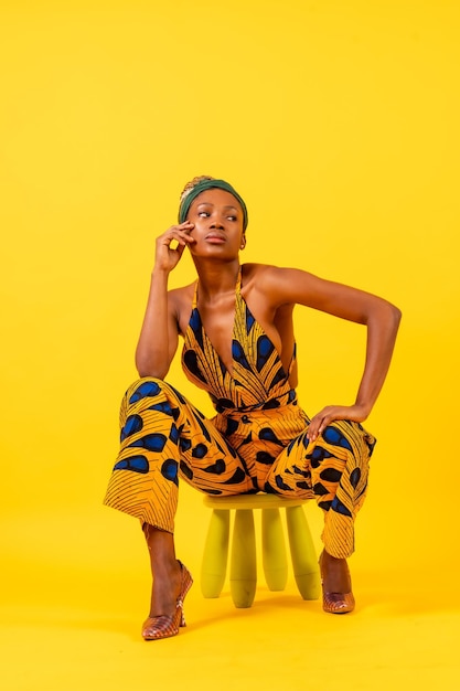 Młoda Afrykańska kobieta w tradycyjnej sukience na żółtym tle siedzi w fotografii komercyjnej