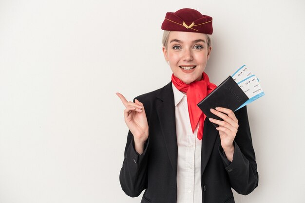 Młoda Air Hostess Kaukaski Kobieta Paszport Na Białym Tle Uśmiecha Się I Wskazuje Na Bok, Pokazując Coś W Pustej Przestrzeni.