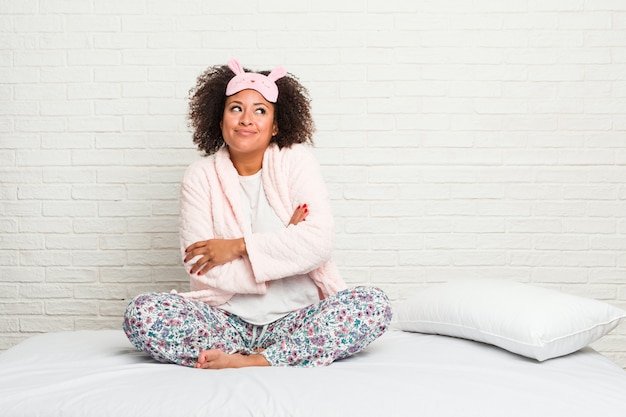 Młoda amerykanin afrykańskiego pochodzenia kobieta jest ubranym pijama w łóżku ono uśmiecha się ufny z krzyżować rękami.