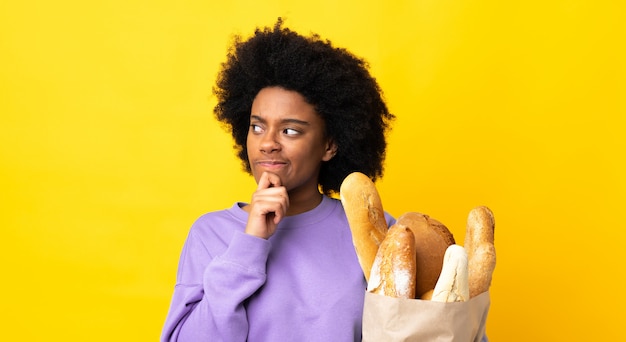Młoda Amerykanin Afrykańskiego Pochodzenia Kobieta Kupuje Coś Chleb Odizolowywającego Na żółtym Tle Ma Wątpliwości I Główkowanie