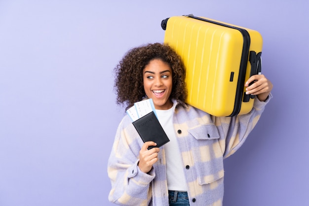 Młoda amerykanin afrykańskiego pochodzenia kobieta na purpurach izoluje w wakacje z walizką i paszportem