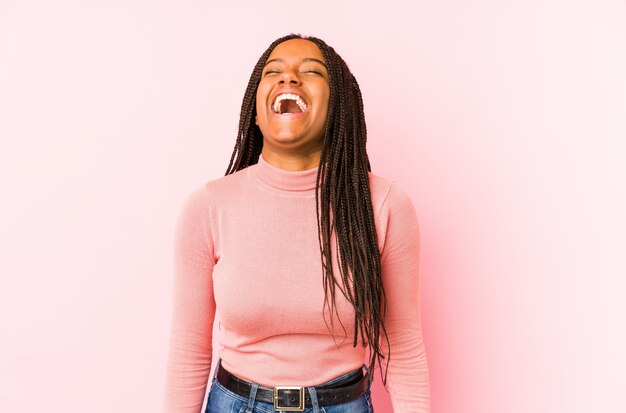 Młoda amerykanin afrykańskiego pochodzenia kobieta odizolowywająca na różowej ścianie zrelaksowany i szczęśliwy śmia się, szyja rozciągająca pokazuje zęby.