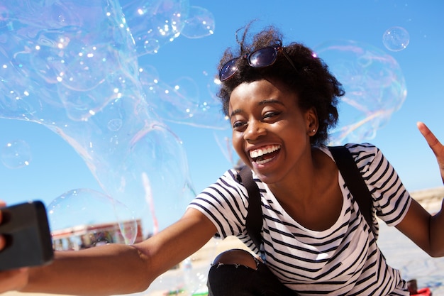 Młoda amerykanin afrykańskiego pochodzenia kobieta opowiada selfie outdoors z dużymi mydlanymi bąblami